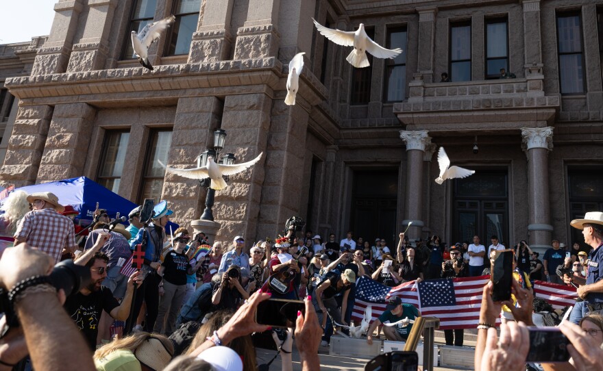 Democracy rally at the Texas State Capitol with doves flying overhead, showing community members gathered with American flags in peaceful demonstration